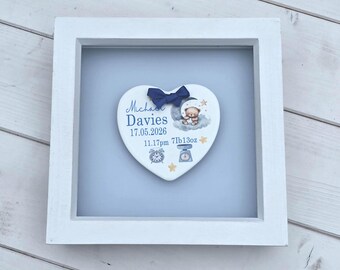 May include: A white square shadow box frame containing a heart-shaped plaque with a navy blue bow. The plaque features the text Michael Davies, 17.05.2026, 11.17pm, 7lb13oz, a teddy bear on a cloud, a clock, a scale, and gold stars.