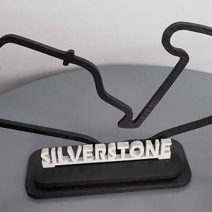 May include: Black wooden model of the Silverstone racetrack with the name "SILVERSTONE" printed in white on a black base.
