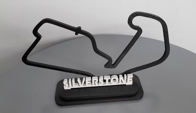 May include: Black wooden model of the Silverstone racetrack with the name "SILVERSTONE" printed in white on a black base.