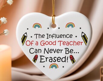 May include: White heart-shaped ornament with a gold hanging string. The ornament has the text "The Influence Of a Good Teacher Can Never Be... Erased!" and rainbow and pencil designs. A lovely gift for teachers.