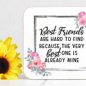 May include: A white square sign with the text "Best Friends are hard to find because the very best one is already mine." The sign has a black border and floral accents. Yellow sunflowers are in the foreground.