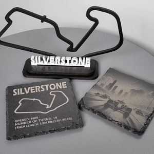 May include: Black and white image of the Silverstone race track on a slate coaster. The coaster has the words "SILVERSTONE" printed on it. The text below the track image reads "OPENED: 1969, NUMBER OF TURNS: 18, TRACK LENGTH: 5.891 KM (3.661 MILES)".