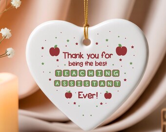 May include: White heart-shaped ornament with gold string, featuring the text "Thank you for being the best TEACHING ASSISTANT Ever!" in green and red. Decorated with red apple and green star graphics. A thoughtful gift.
