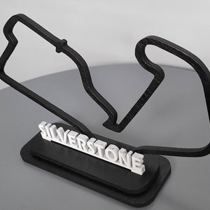 May include: A black wooden model of the Silverstone racetrack with the name "Silverstone" in white letters on a black base.