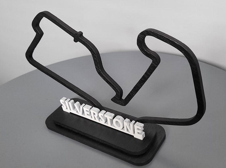 May include: A black wooden model of the Silverstone racetrack with the name "Silverstone" in white letters on a black base.