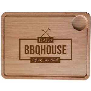 May include: A wooden chopping board with a juice groove and a round indentation for a serving dish. The board is engraved with the text "DAD'S BBQHOUSE I Grill, You Chill" and a crossed grill utensil graphic.