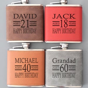 Op de afbeelding: Vier gepersonaliseerde heupflacons met zilveren doppen. De flacons zijn bruin, rood, oranje en grijs. Elke flacon heeft een gegraveerde naam en leeftijd, met de woorden "Happy Birthday" eronder. De bruine flacon zegt "David aged 21 years".