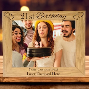 May include: A wooden photo frame with the text "21st Birthday" engraved on the top. The frame has two hearts on either side of the text. The frame is holding a photo of four people celebrating a birthday. The photo shows a person blowing out candles on a cake.