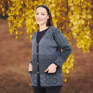 May include: A long-sleeved, button-down cardigan featuring a grey and black geometric pattern. The garment includes a V-neckline, two front patch pockets, and a solid black trim along the button placket, cuffs, and pocket edges, worn over a black top.