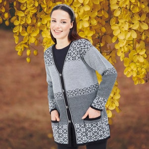 May include: A long-sleeved button-down cardigan featuring a black and white geometric pattern with horizontal bands of varying textures. The garment includes a solid black trim along the V-neckline, front placket, and two front patch pockets.