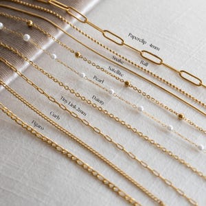 May include: A collection of gold-toned metal chains labeled as Paperclip 4mm, Snake, Ball, Satellite, Pearl, Dainty, Tiny Link 2mm, Curb, and Figaro. Each chain features a distinct link style, with some incorporating small white beads.