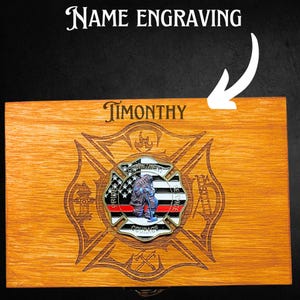 K&ouml;nnte beinhalten: Eine Holzkiste mit einem eingravierten Feuerwehr-Emblem auf dem Deckel. Das Emblem zeigt einen Feuerwehrmann mit Helm und einer roten Linie in der Mitte. Die Worte "Stolz", "Mut", "Engagement" und "Dienst" sind um das Emblem herum eingraviert. Die Box ist mit dem Namen "TIMONTHY" auf der Oberseite personalisiert.