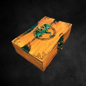 May include: A wooden box with a green dragon design on the lid. The box has a brass latch and intricate carvings around the edges.