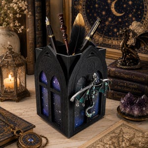 May include: Black pen holder with a gothic arch design. The holder features a starry night background visible through the arched windows. A decorative dragon is attached to the side. Pens and a feather are inside the holder.