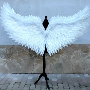 May include: White feathered angel wings on a black stand. The wings are large and have a delicate, layered look.