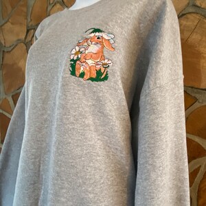May include: Gray sweatshirt with an embroidered image of a brown bunny sitting in a field of white flowers.