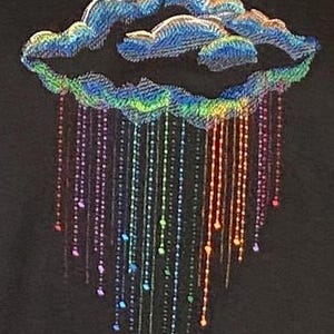 May include: A decorative cloud design with rainbow-coloured rain. The cloud is blue with iridescent detailing, and the rain is made of strings of beads in various colours. The background is black.