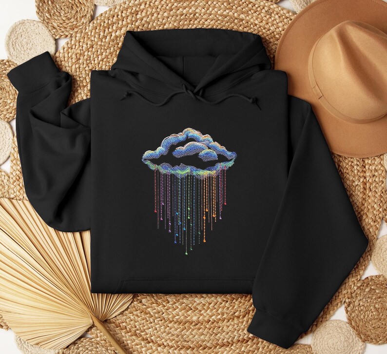 May include: Black hoodie with a cloud design and colourful rain. The cloud is outlined in blue and the rain is made of colourful strings with small beads. The sweatshirt is made of a soft material.
