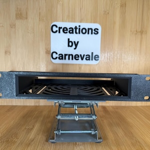 May include: Black metal rack with a rectangular opening and a black metal grate inside. The rack is sitting on a silver metal stand with adjustable legs. The text "Creations by Carnevale" is visible on a white label.