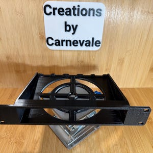May include: Black plastic 3D printed fan mount with a circular opening and a grid pattern. The mount is designed to fit a standard computer fan.