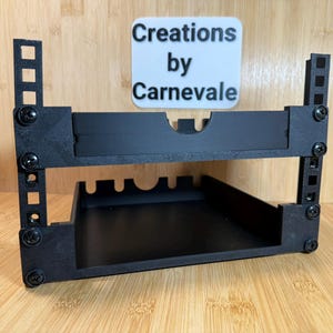 May include: Black, two-tiered shelf with a rectangular base and vertical supports. The shelf has a cutout on the top tier and several slots on the bottom tier. The text "Creations by Carnevale" is on a white background above the shelf.