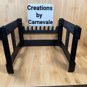 May include: Black metal rack with multiple slots for holding items. The rack is made of metal and has a black finish. The rack is empty and is sitting on a wooden surface.