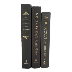 May include: Three black hardcover books stacked vertically. The titles are "The Starless Sea" by Erin Morgenstern, "No Easy Day" by Mark Owen with Kevin Maurer, and "My Sister's Keeper" by Jodi Picoult.