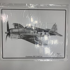 May include: Black and white pencil drawing of a Grumman F6F Hellcat airplane. The aircraft is seen in profile, with the number "M7" and stars on the wings. The text "Grumman F6F 5 Hell Cat" is printed at the bottom.