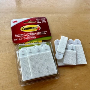 K&ouml;nnte beinhalten: Eine Packung 3M Command Damage-Free Hanging Streifen im Value Pack. Die Packung enth&auml;lt 8 Paare wei&szlig;e Streifen, die f&uuml;r eine Tragkraft von bis zu 5,4 kg ausgelegt sind. Die Streifen sind in der Verpackung und auch auf einer Holzoberfl&auml;che ausgelegt.