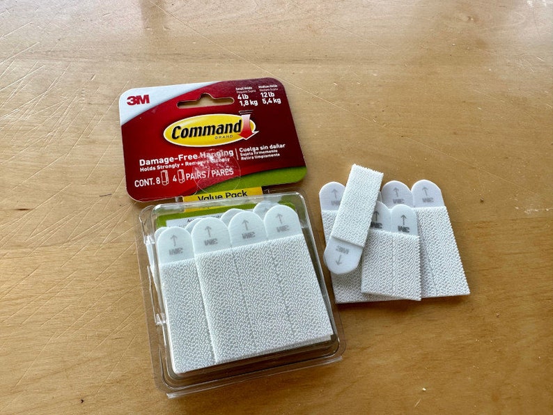 K&ouml;nnte beinhalten: Eine Packung 3M Command Damage-Free Hanging Streifen im Value Pack. Die Packung enth&auml;lt 8 Paare wei&szlig;e Streifen, die f&uuml;r eine Tragkraft von bis zu 5,4 kg ausgelegt sind. Die Streifen sind in der Verpackung und auch auf einer Holzoberfl&auml;che ausgelegt.