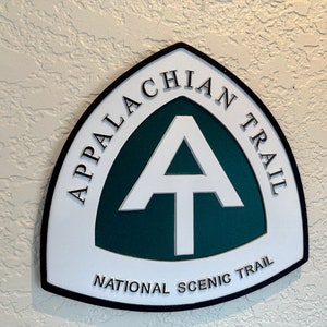 K&ouml;nnte beinhalten: Ein wei&szlig;es und gr&uuml;nes Schild mit schwarzer Beschriftung, auf dem "Appalachian Trail National Scenic Trail" steht. Das Schild zeigt ein wei&szlig;es "A" mit einer wei&szlig;en Linie oben, innerhalb eines gr&uuml;nen Kreises.