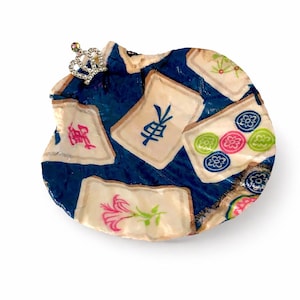 May include: A decorative, round object with a dark blue background and several off-white tiles. The tiles feature colorful designs and Chinese characters. A small, jeweled crown is attached to the top. The object has a unique, handmade appearance.