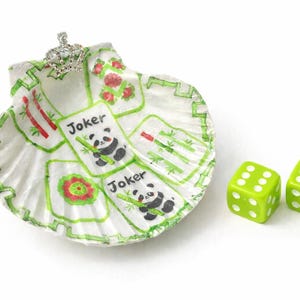 May include: A hand-painted seashell dish with a silver crown and two green dice. The dish features panda and bamboo card designs with the word "Joker". The dice have white dots.