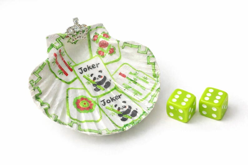 May include: A hand-painted seashell dish with a silver crown and two green dice. The dish features panda and bamboo card designs with the word "Joker". The dice have white dots.