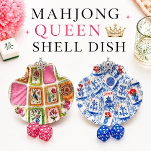 May include: Two shell-shaped dishes decorated with Mahjong tile patterns. One dish features pink and green floral motifs, the other blue and white floral designs. Each dish is topped with a small silver crown and paired with two dice.
