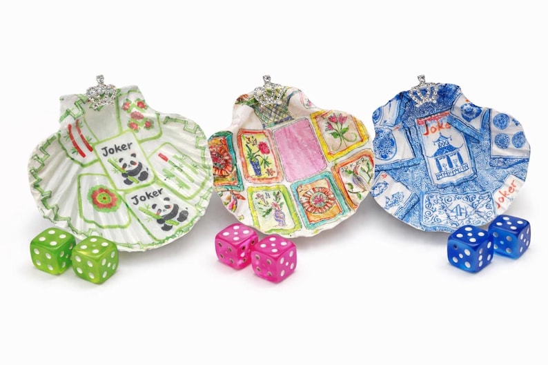 May include: Three decorative seashell dishes with hand-painted designs. One features panda bears and the word "Joker", another has floral and card motifs, and the third has a blue and white design. Each shell is adorned with a jeweled crown and accompanied by dice.