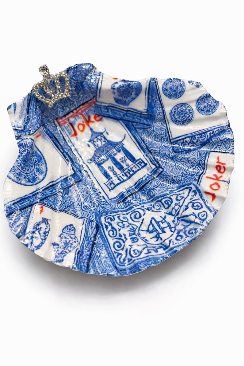 May include: A decorative, shell-shaped dish with a blue and white playing card design. The dish features a small, jeweled crown and the word "Joker" in red. The design includes images of pagodas and card suits.