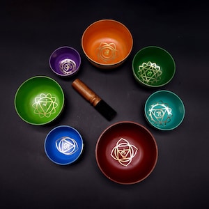 Może przedstawiać: Siedem śpiewających mis z różnymi szkliwami i złotymi symbolami. Misy są ułożone w kółko na czarnym tle. W środku koła znajduje się drewniany młotek.