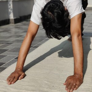 K&ouml;nnte beinhalten: Eine Person macht eine Yoga-&Uuml;bung in der Haltung des nach unten gerichteten Hundes auf einer wei&szlig;en Yogamatte.