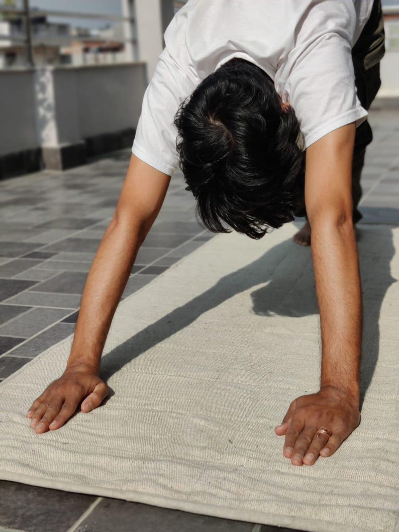 K&ouml;nnte beinhalten: Eine Person macht eine Yoga-&Uuml;bung in der Haltung des nach unten gerichteten Hundes auf einer wei&szlig;en Yogamatte.