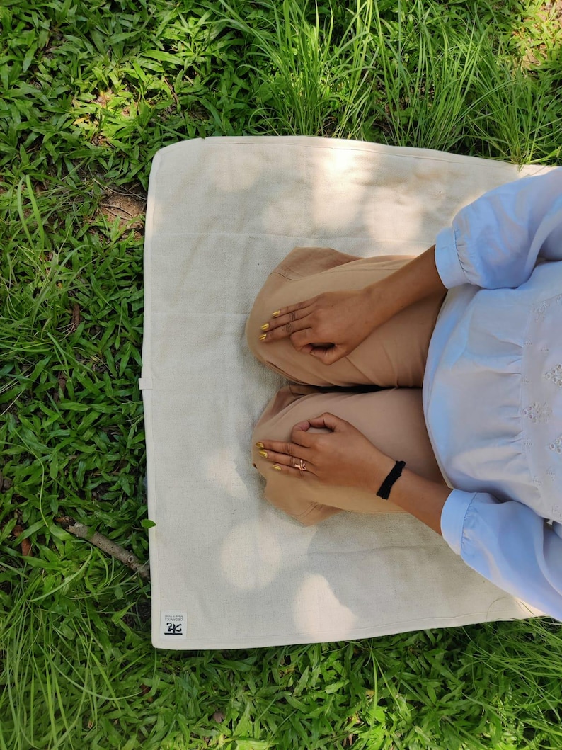 K&ouml;nnte beinhalten: Eine Person sitzt auf einer wei&szlig;en Baumwolldecke mit einem braunen Stofflabel, auf dem "2F" steht. Die Person tr&auml;gt ein hellblaues Hemd und eine braune Hose. Die Decke liegt auf einem Bett aus gr&uuml;nem Gras.
