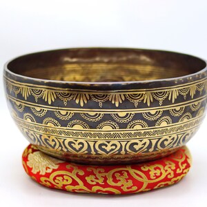 May include: A black singing bowl with gold decorative patterns and a red cushion with gold embroidery.