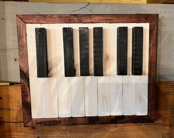 Puede incluir: Una pieza de arte de pared de madera con forma de teclado de piano. Las teclas negras están hechas de madera oscura y las teclas blancas están hechas de madera clara. La pieza está enmarcada en madera oscura.