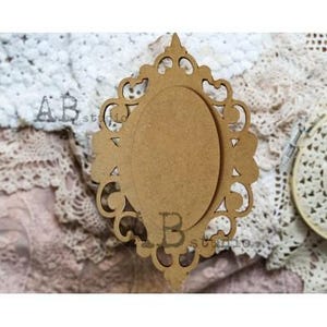 May include: A decorative wooden frame with an oval center and ornate, openwork edges. The frame is a natural wood color and has the text "AB studio" and "B" on it. The frame is likely for crafts or home decor.
