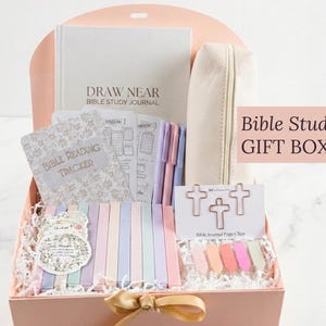 May include: A pink gift box filled with Bible study supplies. Includes a journal, tracker, pens, page clips, and a pencil case. The box has the text "Bible Study GIFT BOX" on the side.
