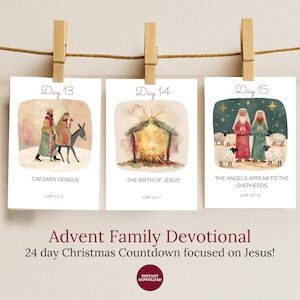 May include: Advent Family Devotional cards, each clipped to a string with wooden clothespins. The cards feature watercolor illustrations of biblical scenes, including Caesar's Census, the Birth of Jesus, and the Angels appearing to the Shepherds.
