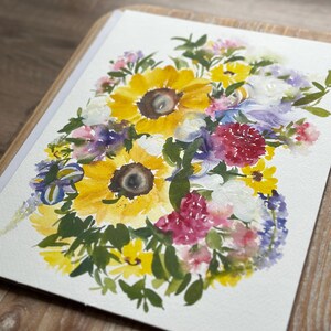 May include: A watercolor painting on white paper featuring a vibrant floral arrangement. The composition includes large yellow sunflowers with dark centers, interspersed with smaller pink, purple, and white blossoms, surrounded by green foliage.