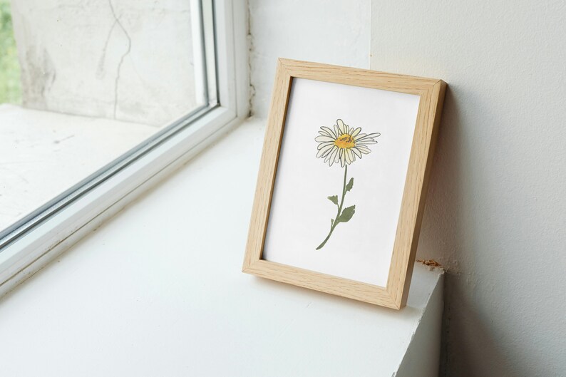 Pu&ograve; includere: Una stampa incorniciata di una margherita bianca con un centro giallo, su sfondo bianco. La cornice &egrave; in legno chiaro.