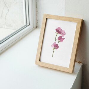 May include: A framed watercolor painting of a pink flower with a green stem. The painting is in a light wood frame.