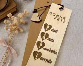 May include: A wooden bookmark with the words "BONNE FETE" and the letters PAPI in heart shapes, along with a mustache design. The bookmark is light brown and has a small heart-shaped charm attached.